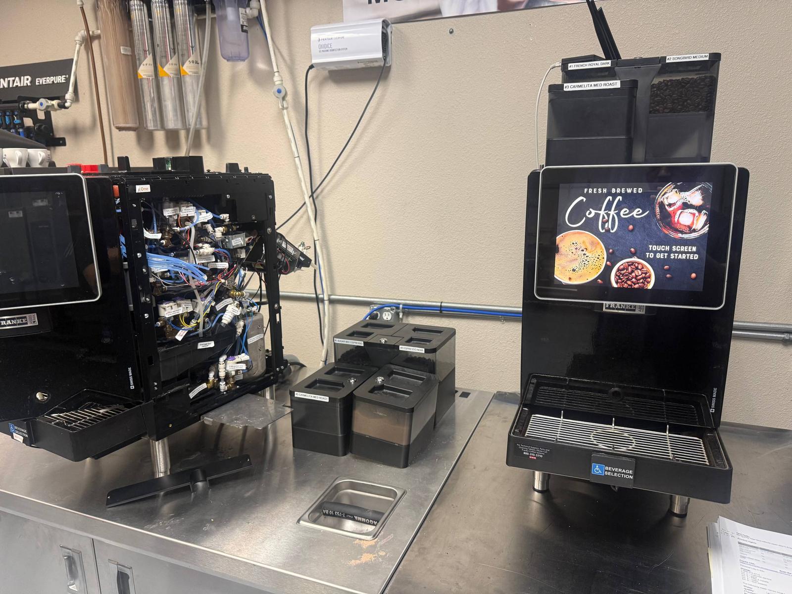 An open Franke A-Series machine beside another coffee machine on a worktable